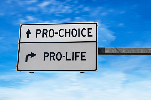 White two street signs with arrow on metal pole on blue sky background. Female right on abortion