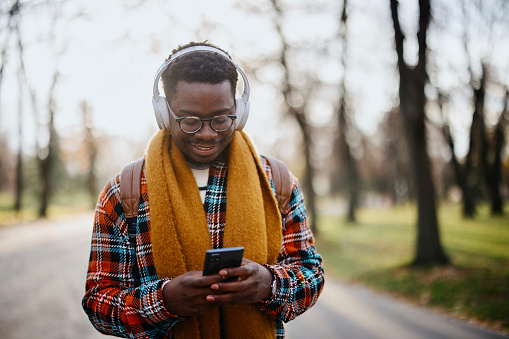 Young black man walking in the park while listening to the music on his wireless headphones
