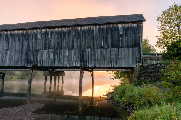 istock Weathered covered bridge over calm misty water at sunrise 1367702894