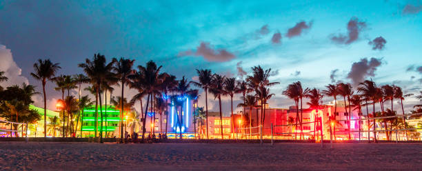 panorama do miami beach ocean drive com hotéis e restaurantes ao pôr do sol. horizonte da cidade com palmeiras à noite. vida noturna art déco na praia sul - miami beach - fotografias e filmes do acervo