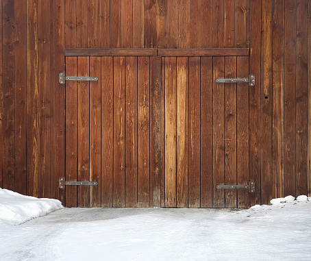 Old wooden gates, iron hinges in snow. Faded, unpainted gates