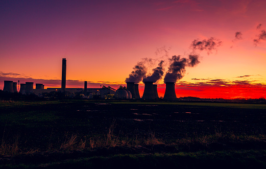 Silhouette of a power station against a stunning and colourful winter sunrise near Drax in North Yorkshire, UK with plumes of water vapour rising from the cooling towers.