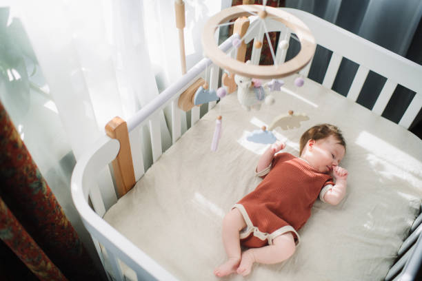 Cute baby girl in her crib Newborn girl lies in white cradle with mobile above jumpsuit stock pictures, royalty-free photos & images