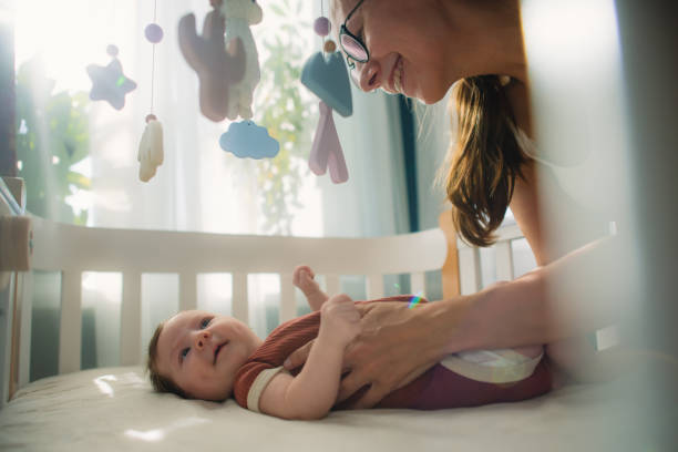 mother with her cute baby girl in her crib - using mobile imagens e fotografias de stock