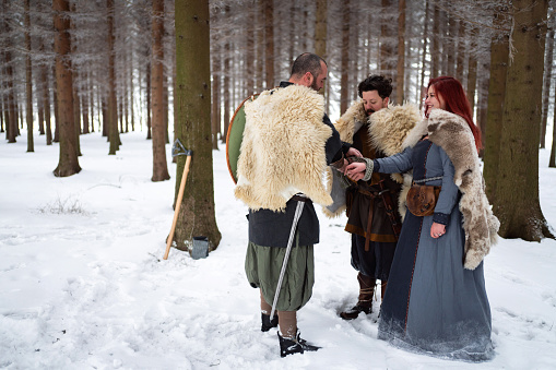 Medieval priest maintains the marriage ceremony between male and female medieval warriors, in the snowy forest during winter