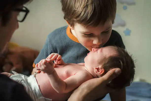Photo of Little boy kissing his newborn sister