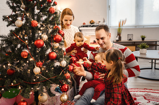 Happy family with three daughters decorating Christmas tree in living room