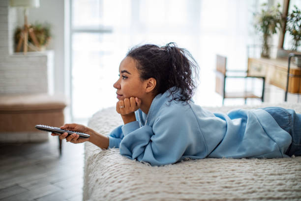 Giovane donna africana che guarda la TV a casa - foto stock