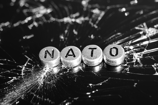 NATO inscription on the background of broken glass. Black and white photo.