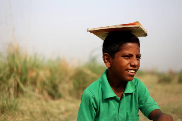 Elementary age poor child of Indian ethnicity holding book on his head outdoor in nature.
