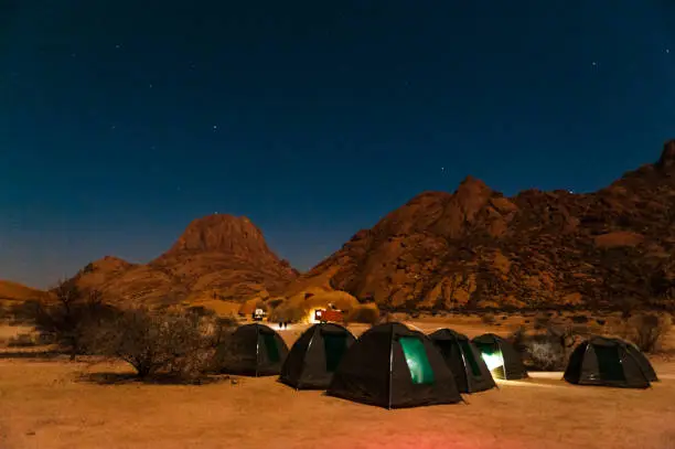 Night shot of an assembly of tents on a campground in the desert of Namibia. The night sky is filled with stars.
