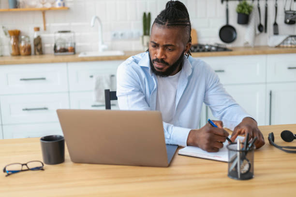 istock Focused African American man uses laptop computer for online learning remotely at home taking notes on notepad during online lesson 1367719828