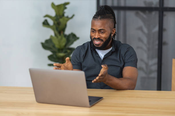 istock Successful African American man using laptop to communicate with colleagues or client via video conference while sitting at table in office, smiling 1367720400