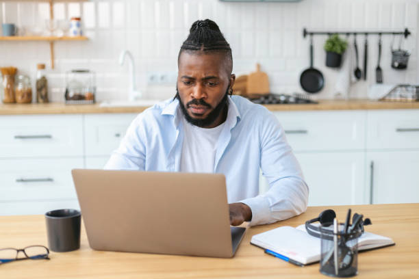 istock Thoughtful African American man working remotely at home using laptop computer. Work outside the office concept 1367720401