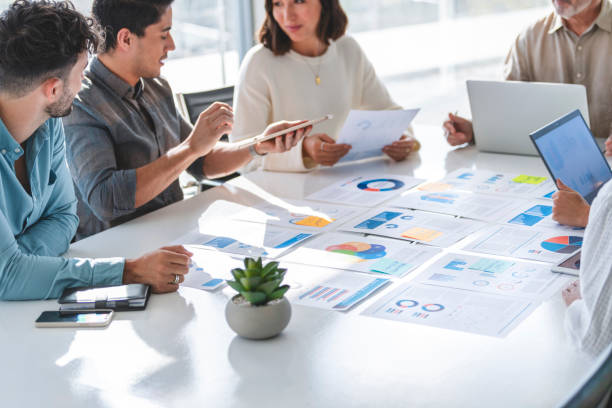 istock Multi racial group of people working with Paperwork on a board room table at a business presentation or seminar. 1367721695