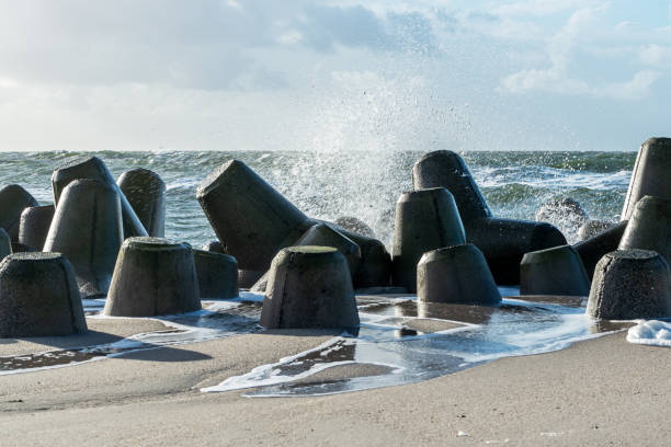 onde che colpiscono i tetrapodi di cemento frangiflutti sulla spiaggia - sea defence concrete foto e immagini stock