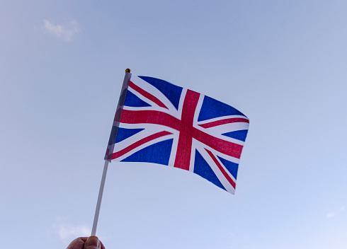 Hand holding a hand held Union Jack flag and waving it, blue sky background for Jubilee celebrations
