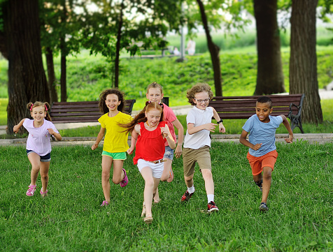 a group of children of boys and girls of different races are running on the green grass against the background of a recreation park. Children's Day, Friendship of Nations.