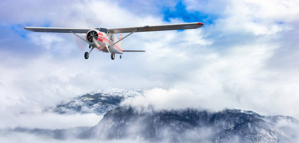 A small aircraft is seen in flight against the backdrop of steep, forested mountains. The scene highlights the expansive wilderness and the concept of remote travel or adventure tourism.