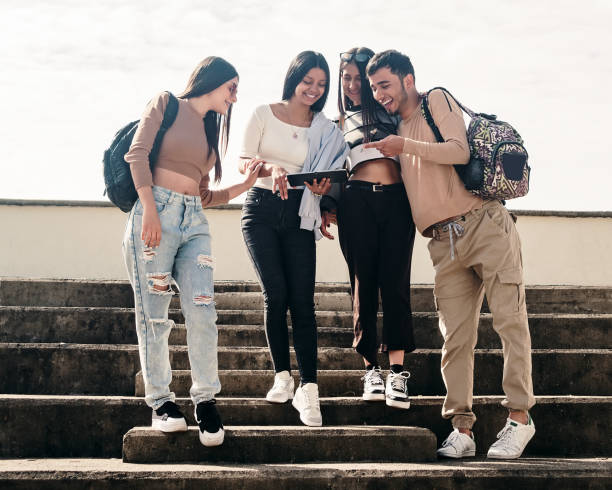College friends smiling while looking at something on a tablet stock photo
