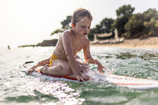 Photo of little boy trying to surf on a surfboard with a little help by his mother