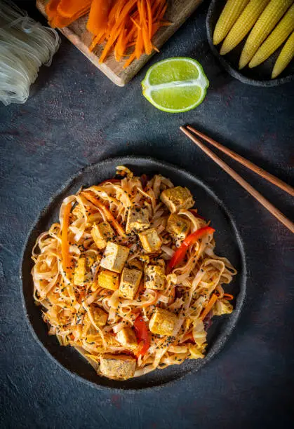 Pad thai vegetarian plant based Asian recipe with ingredients as rice noodles, tofu, garlic, shallots, onion, hot chili, radish, sauerkraut, carrot, red bell pepper, cabbage, bean sprouts, soy sauce, sriracha hot sauce and lime.