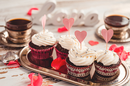 Buttercream cupcakes decorated with silver candies and paper hearts close-up. Soft focus