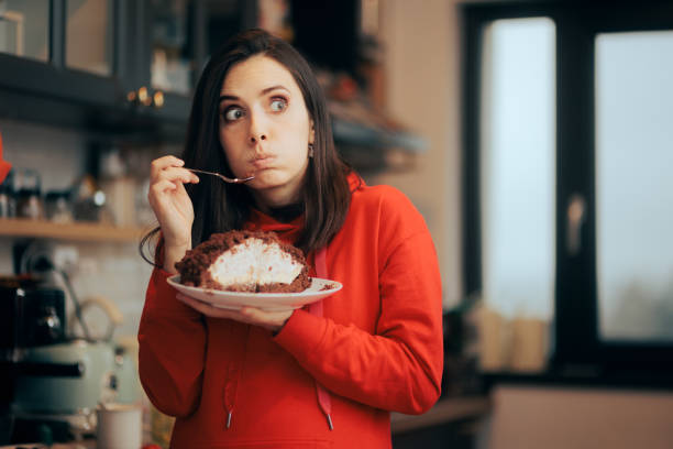 mujer divertida que se siente culpable comiendo pastel trampa dieta - codicia fotografías e imágenes de stock