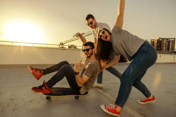 Three friends having fun while guy sitting on skateboard at sunset