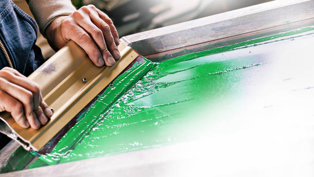 serigraph printing production. silk screen textile printery. male hand with a squeegee. creating print on t-shirt in workshop