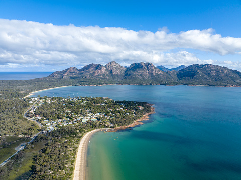 High angle aerial drone view of Coles Bay with Richardsons Beach and Hazards mountain range in the background, part of Freycinet Peninsula National Park, Tasmania, Australia. Muirs Beach in foreground