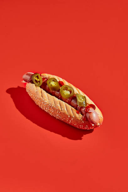 American hot dog with jalopeno on red background minimal style. Fast food on colour background with hard shadow. Sandwich with sausage trendy concept. American hot dog with jalopeno on red background minimal style. Fast food on colour background with hard shadow. Sandwich with sausage trendy concept hot dog photos stock pictures, royalty-free photos & images