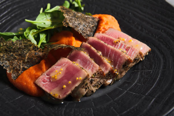 thunfischsteak mit tomatensalsa, spinat und nori auf schwarzem teller. leckeres fischgericht aus thunfischscheibenförmig auf tomatensauce im dunklen stil. moderne speisekarte. hauptgericht des fisches. - raw tuna steak marinated sauces stock-fotos und bilder