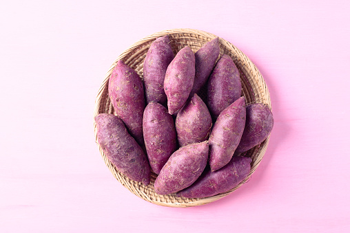 Purple sweet potatoes in basket on pink background, Top view
