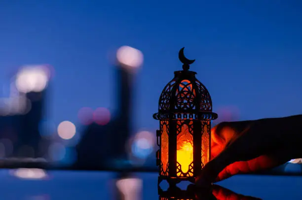 Selective focus of lantern that have moon symbol on top holding by hand with city background for the Muslim feast of the holy month of Ramadan Kareem.