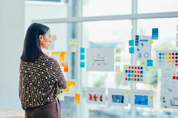 plan de recul d’un jeune designer en train de réfléchir avec des notes sur un mur de verre dans un bureau - advertisement photos et images de collection