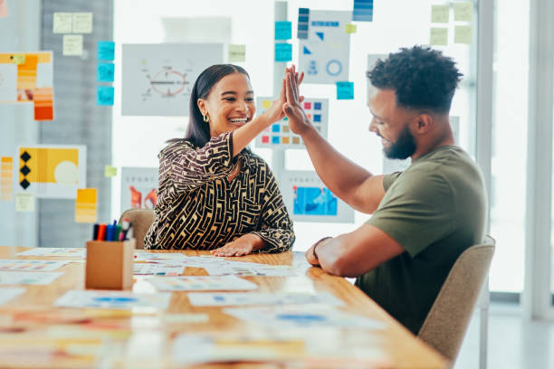 foto de dos jóvenes diseñadores dándose un alto cinco mientras trabajan juntos en una oficina - branding marketing strategy business fotografías e imágenes de stock