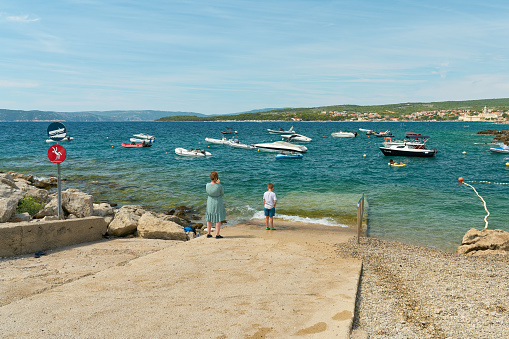 Krk, Croatia – August 04, 2021: Holidaymakers on the beach of the Adriatic Sea in Croatia. In the background the old town of Krk.