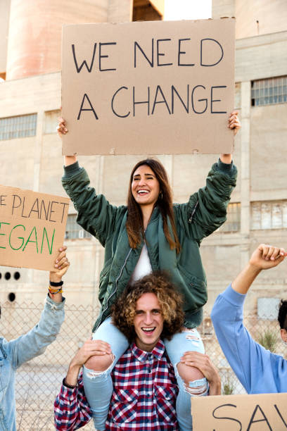 glückliche junge hispanische frau, die auf der schulter eines mannes sitzt und gegen den klimawandel protestiert. vertikales bild - cardboard sign stock-fotos und bilder