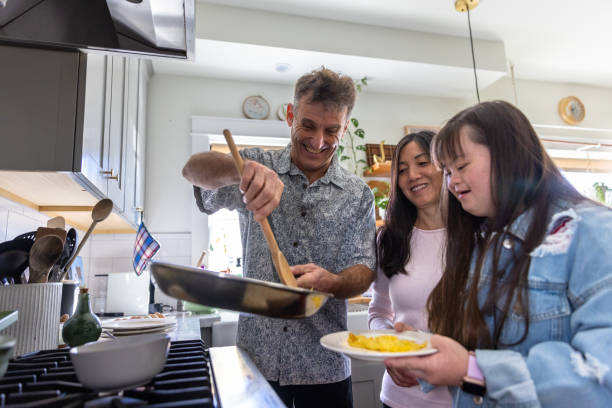Family making breakfast together in kitchen, the daughter has Down's Syndrome stock photo