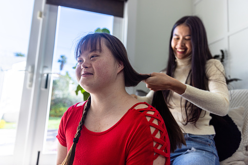 Diverse sisters doing hair, one has Down’s syndrome.