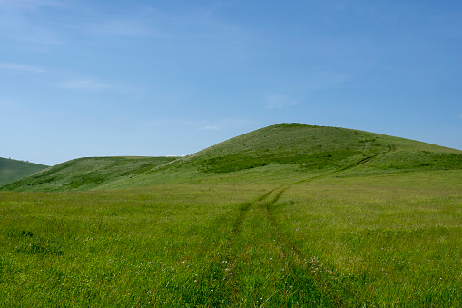 Beautiful summer landscape of green hills against the background of a blue sky. Dirt road in the steppe.