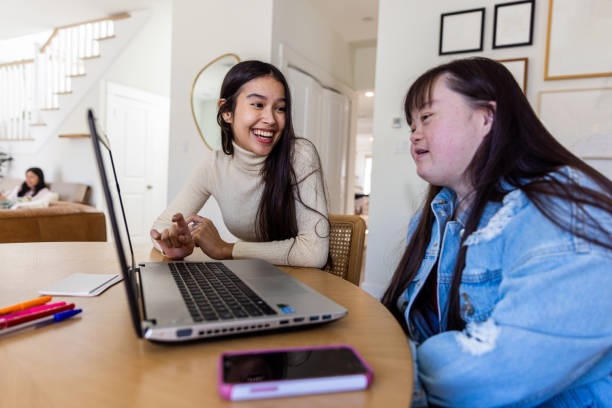 Sisters Studying together on laptop. One sister has Down's Syndrome. stock photo