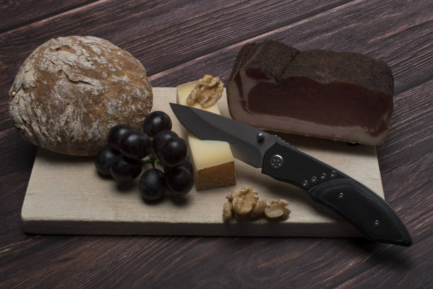 savory tasty loin bacon cheese grapes walnuts traditional South Tyrolean bread and snack knife on light wooden board in front of dark wooden background