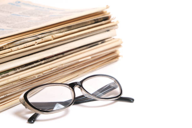 istock Stack of old newspapers and reading glasses on a white background. 1367778525