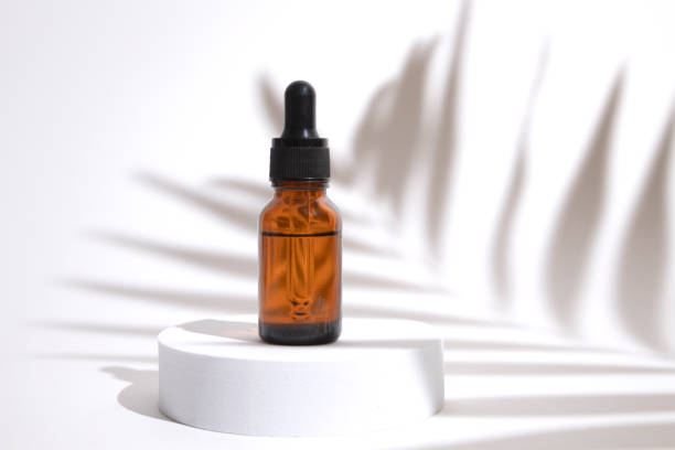 istock Glass dropper bottle on podium with shadow palm leaves. Cosmetic container mock-up. Creative minimalistic shot of a cosmetic product. Spa concept. Mock-up bottle for branding and label 1367779659