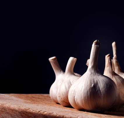 garlic bulbs on rustic wooden cutting board. still life with dark copyspace. Aromatic food ingredients on kitchen table with black background. Garlic cloves spice prepared for cooking.