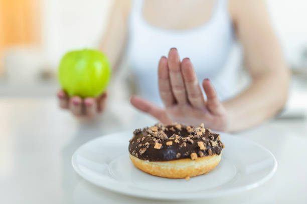 ダイエットや良い健康の概念。ジャンク フードやドーナツなどデザートの不健康な食べ物を拒否し、新鮮な果物や野菜などの健康食品を選択する若い女性。 - chocolate candy chocolate candy plate ストックフォトと画像