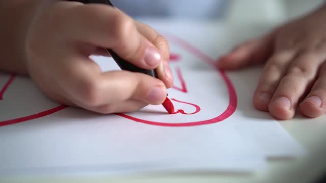 Child draws hearts on paper with pink markers. Close-up. Children's creativity. St. Valentines day