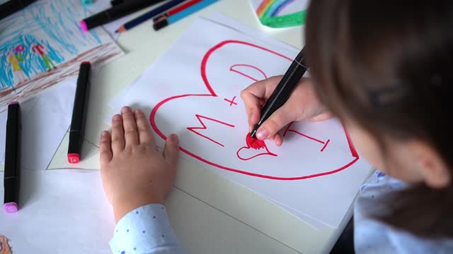 Child draws hearts on paper with pink markers. Children creativity. St. Valentines day, happy family
